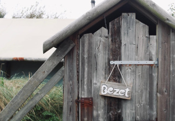 Porta di legno con cartello 'Bezet' presso un alloggio glamping, circondata da natura e una tenda.