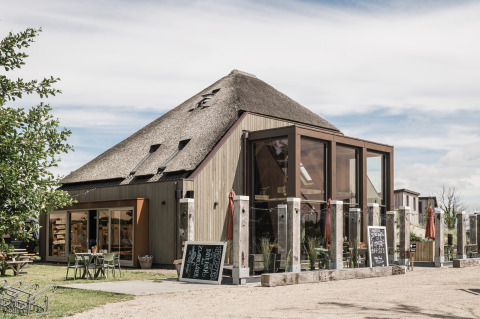 Foto van een moderne glampingaccommodatie met rieten dak, grote glazen ramen en buitenterras.