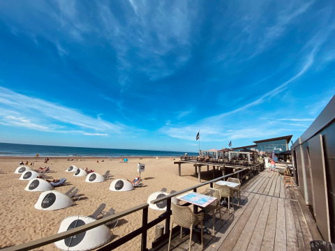 Glamping en la playa con tiendas modernas, huéspedes relajados y restaurante con terraza frente al mar soleado.