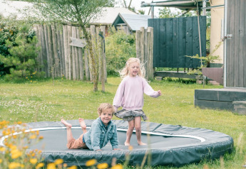 Due bambini giocano su un trampolino interrato circondato da fiori selvatici in un alloggio glamping.