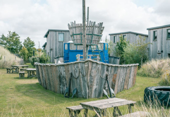 Photo d’un hébergement glamping avec une aire de jeux en bois en forme de bateau, entourée de cabanes et d’herbe.