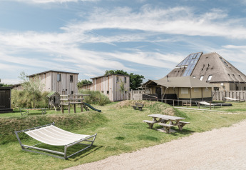 Foto exterior de un albergue moderno con cabañas de madera, mesas de picnic, hamacas y área de juegos.