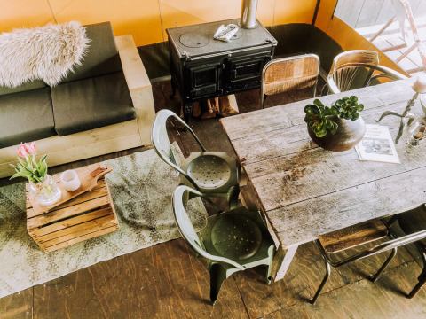 Hyggeligt interiør med rustikt spisebord, brændeovn, sofa, stole og planter på Beach Lodge Luxury.