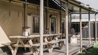 Außenterrasse mit Holzbänken am Beach Lodge Luxury im Duynpark Het Zwanenwater, Niederlande, sonnig.