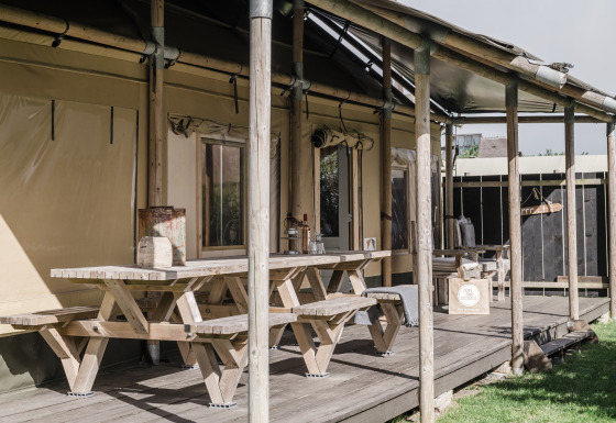 Terrazza in legno con tavoli e panche al Beach Lodge Luxury, Duynpark Het Zwanenwater, Paesi Bassi, al sole.