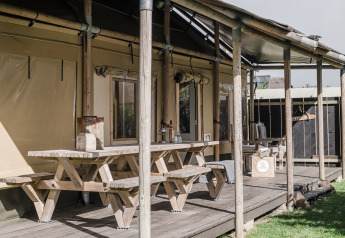 Terraza de madera con bancos en Beach Lodge Luxury en Duynpark Het Zwanenwater, Países Bajos, día soleado.