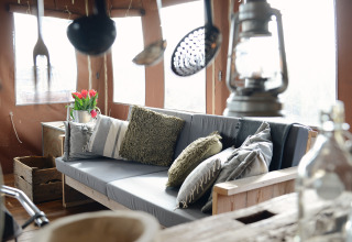 Gezellig lodge-interieur met sofa, kussens, lantaarn en bloemen bij Duynlodge in Duynpark Het Zwanenwater.