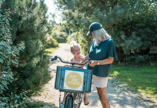 Mujer con niña disfruta de un día soleado paseando una bicicleta entre naturaleza en un sitio de glamping.