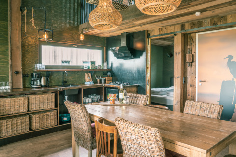 Rustieke keuken en eethoek in de Juttershut lodge bij Duynpark Het Zwanenwater, Nederland, met rotan stoelen.