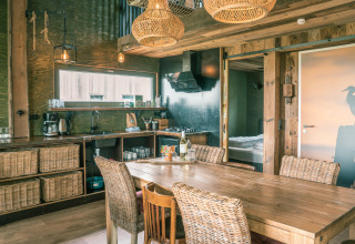 Rustieke keuken en eethoek in de Juttershut lodge bij Duynpark Het Zwanenwater, Nederland, met rotan stoelen.