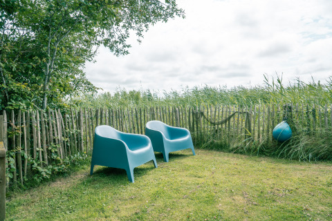 Dos sillas azules en un jardín con cerca de madera en Juttershut lodge, Duynpark Het Zwanenwater, Países Bajos.