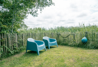 Due sedie blu in giardino con staccionata di legno al lodge Juttershut, Duynpark Het Zwanenwater, Paesi Bassi.