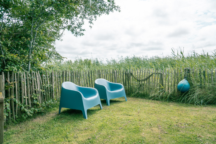 Zwei blaue Stühle im Garten, umgeben von grünem Zaun am Juttershut-Lodge, Duynpark Het Zwanenwater.
