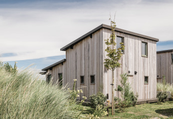 The Juttershut lodge at Duynpark Het Zwanenwater in the Netherlands, surrounded by greenery and clear skies.
