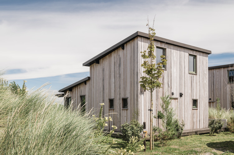Die Lodge Juttershut im Duynpark Het Zwanenwater in den Niederlanden, umgeben von Pflanzen und blauem Himmel.