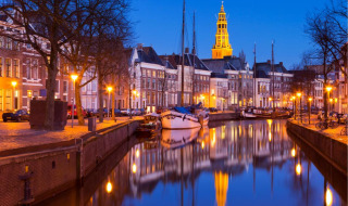 Vista nocturna de un canal en Groningen, Países Bajos, con barcos y un campanario iluminado al fondo.