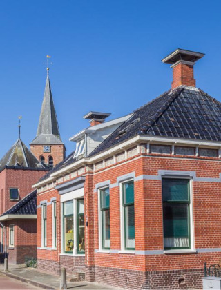 Vista de calle en Oostwold, Groningen, Países Bajos, con casas tradicionales de ladrillo y cielo despejado.