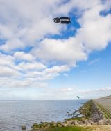 Persona practicando kitesurf en aguas cercanas a Oostwold, Groningen, con cielo azul y nubes blancas.