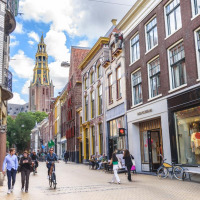 Personas pasean y andan en bicicleta por una calle colorida de Groningen, Países Bajos, con una torre de iglesia.
