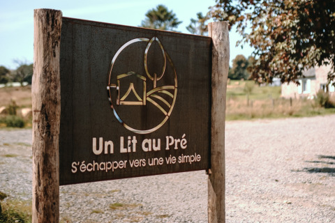 Cartel en Feather Down Ô manoir de Glams, parque vacacional en Normandía, Francia, con el texto 'Un Lit au Pré'.