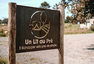 Cartel en Feather Down Ô manoir de Glams, parque vacacional en Normandía, Francia, con el texto 'Un Lit au Pré'.