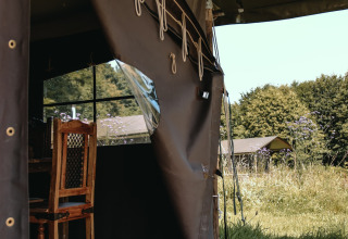 Blick aus einem Zelt im Feather Down Ô manoir de Glams mit Holzstuhl und Natur in der Normandie.
