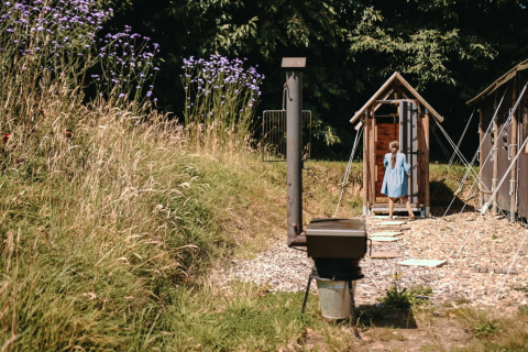 Una niña con vestido azul entra a una cabaña de madera en Feather Down Ô manoir de Glams en Normandía, Francia.