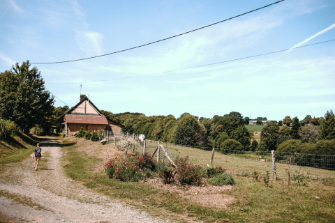 Eine Person geht einen Feldweg entlang zu einem Haus im Grünen bei Feather Down Ô manoir de Glams in der Normandie, Frankreich.