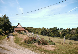 Eine Person geht einen Feldweg entlang zu einem Haus im Grünen bei Feather Down Ô manoir de Glams in der Normandie, Frankreich.