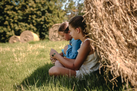 Twee kinderen zitten in het gras bij een grote hooibaal op Feather Down Ô manoir de Glams in Normandië, Frankrijk.