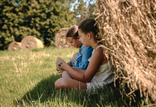 Twee kinderen zitten in het gras bij een grote hooibaal op Feather Down Ô manoir de Glams in Normandië, Frankrijk.