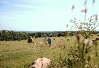 Deux personnes marchent au milieu d’un champ avec des bottes de foin au Feather Down Ô manoir de Glams, Normandie.
