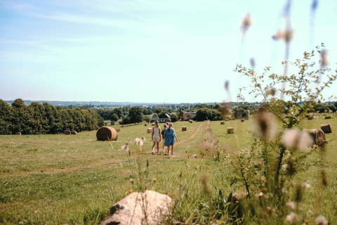 Dos personas caminan por un sendero entre pacas de heno en Feather Down Ô manoir de Glams en Normandía, Francia.