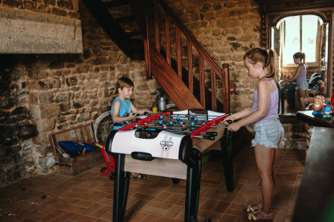 Due bambini giocano a calcetto in una stanza rustica con muri in pietra al Feather Down Ô manoir de Glams in Normandia.