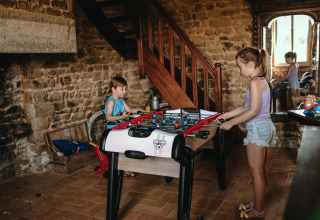 Due bambini giocano a calcetto in una stanza rustica con muri in pietra al Feather Down Ô manoir de Glams in Normandia.