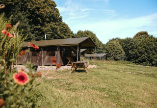 Glamping-telt og picnicbord i Feather Down Ô manoir de Glams, feriested i Normandiet, Frankrig, omgivet af grønne træer.