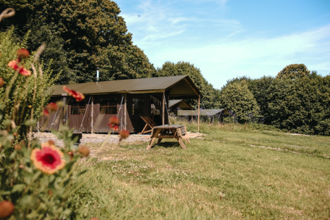 Glamping tent and picnic table at Feather Down Ô manoir de Glams in Normandy, France, surrounded by greenery.