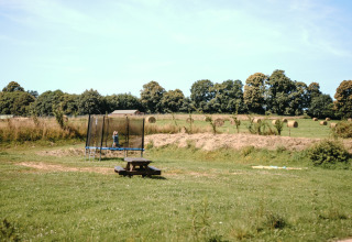 En trampolin, et picnicbord og høballer på en grøn mark ved Feather Down Ô manoir de Glams i Normandiet.