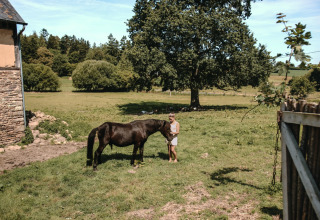 Et barn klapper en sort pony på en grøn mark ved Feather Down Ô manoir de Glams feriepark i Normandiet.