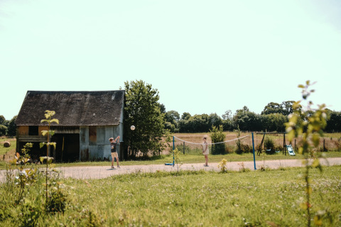 Kinder spielen Badminton neben einer Scheune im Feather Down Ô manoir de Glams, Ferienpark in der Normandie.
