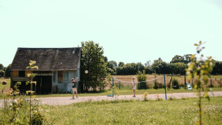 Niños juegan bádminton junto a un granero en Feather Down Ô manoir de Glams, parque vacacional en Normandía.