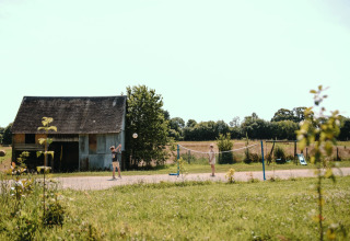Des enfants jouent au badminton près d'une grange à Feather Down Ô manoir de Glams, parc de vacances en Normandie.