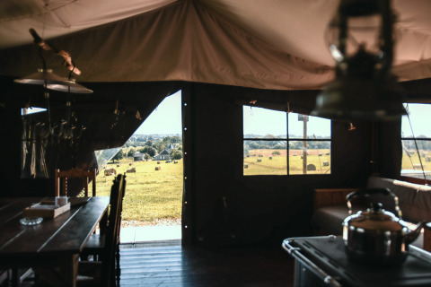 Vista desde el interior de una tienda en Feather Down Ô manoir de Glams en Normandía, Francia, con campos y pacas de heno.
