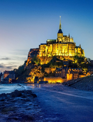 Mont Saint-Michel iluminado al anochecer, visto desde la playa cerca de Isigny-le-Buat en Normandía, Francia.
