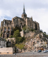 Fotografía de un castillo histórico sobre una colina rocosa cerca de Isigny-le-Buat en Normandía, Francia, con coches abajo.
