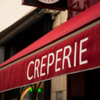 Toldo rojo con la palabra 'CREPERIE' frente a un edificio cerca de Isigny-le-Buat, Normandía, Francia.