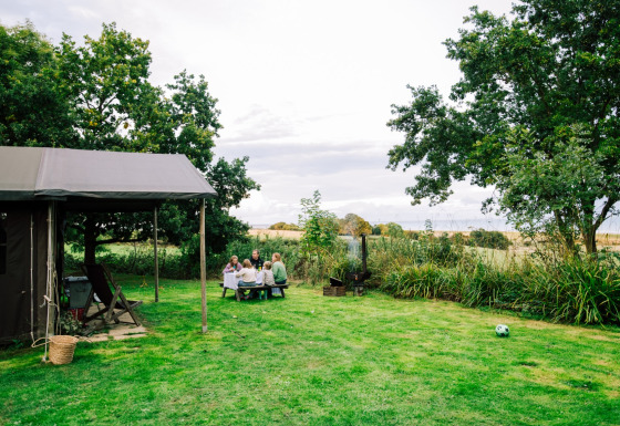 En familie sidder ved et picnicbord i det grønne græs ved Feather Down Lunsford Farm feriepark i Sydøstengland.