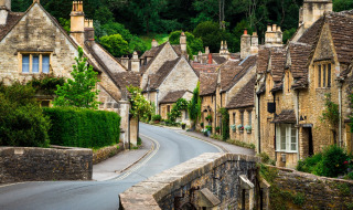 Calle de un pintoresco pueblo bordeada de casas de piedra antigua y abundante vegetación verde alrededor.
