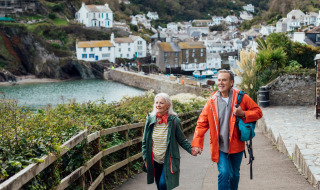 Couple senior marchant main dans la main sur un sentier côtier dans un parc de vacances avec glamping.