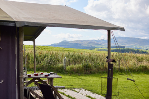 Vista desde una tienda en Feather Down Pant y March Farm, Gales, con mesa de picnic y colinas verdes.